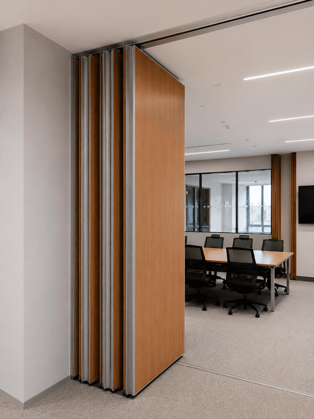 Partially retracted wooden partition wall revealing a modern conference room with table and chairs.